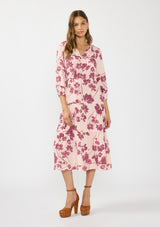 [Color: Coral/Wine] A front facing image of a brunette model wearing a three quarter sleeve midi dress with a pink and burgundy floral print, drawstring waist, and a tiered skirt. Styled with brown platform heels. 