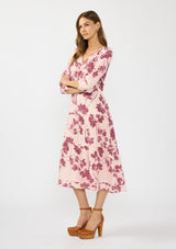 [Color: Coral/Wine] A side facing image of a brunette model wearing a three quarter sleeve midi dress with a pink and burgundy floral print, drawstring waist, and a tiered skirt. Styled with brown platform heels. 