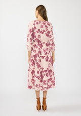 [Color: Coral/Wine] A back facing image of a brunette model wearing a three quarter sleeve midi dress with a pink and burgundy floral print, drawstring waist, and a tiered skirt. Styled with brown platform heels. 