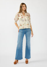 [Color: Ivory/Rosewood] A front facing image of a brunette model wearing an ivory floral print top with puff sleeves, smocked cuffs, smocked neck, and a button front. Styled wit a blue patch pocket denim. 