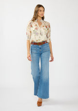 [Color: Ivory/Rosewood] A front facing image of a brunette model wearing an ivory floral print top with puff sleeves, smocked cuffs, smocked neck, and a button front. Styled wit a blue patch pocket denim. 