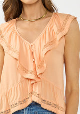[Color: Sorbet] A detail image of a brunette model wearing an orange flutter sleeve top with lace trims, a button front, and a ruffle trimmed hem. Styled with a blue patch pocket denim. 