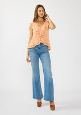 [Color: Sorbet] A front facing image of a brunette model wearing an orange flutter sleeve top with lace trims, a button front, and a ruffle trimmed hem. Styled with a blue patch pocket denim. 