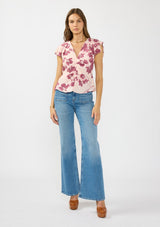 [Color: Coral/Wine] A front facing image of a brunette model wearing a pink and wine floral print top with a ruched center, short flutter sleeves, and a v neckline. 