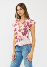 [Color: Coral/Wine] A side facing image of a brunette model wearing a pink and wine floral print top with a ruched center, short flutter sleeves, and a v neckline. 