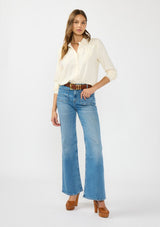 [Color: Natural] A front facing image of a brunette model wearing an off white lace shirt with a collared neck and button front. Tucked into a blue patch pocket denim. 