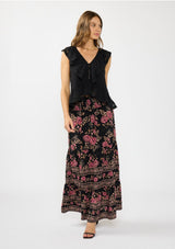 [Color: Black/Dusty Rose] A front facing image of a brunette model wearing a black and pink maxi skirt with a smocked waist and a flowy, tiered silhouette. Styled with a black ruffled top. 