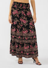 [Color: Black/Dusty Rose] A front facing image of a model wearing a black and pink maxi skirt with a smocked waist and a flowy, tiered silhouette. 