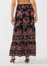 [Color: Black/Dusty Rose] A back facing image of a model wearing a black and pink maxi skirt with a smocked waist and a flowy, tiered silhouette. 