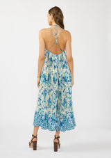 [Color: Natural/Aqua] A back facing image of a brunette model wearing a flowy blue floral maxi dress with a pleated design, scoop neck, halter tie, and front slit. 