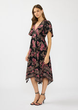 [Color: Black/Dusty Rose] A side facing image of a brunette model wearing a black and pink floral print midi dress with short sleeves, a v neckline, and a handkerchief hemline. 