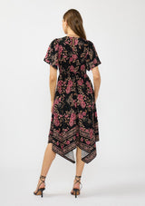 [Color: Black/Dusty Rose] A back facing image of a brunette model wearing a black and pink floral print midi dress with short sleeves, a v neckline, and a handkerchief hemline. 