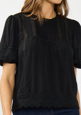 [Color: Black] A detail image of a brunette model wearing a black puff sleeve top with a round neck, lace trims, and pintucks.