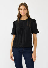 [Color: Black] A front facing image of a brunette model wearing a black puff sleeve top with a round neck, lace trims, and pintucks.