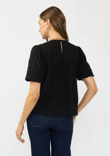 [Color: Black] A back facing image of a brunette model wearing a black puff sleeve top with a round neck, lace trims, and pintucks.