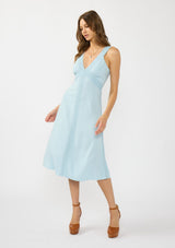 [Color: Blue] A front facing image of a brunette model wearing a light blue sleeveless midi dress with lace trim accents, a v neckline, and an empire waist. 