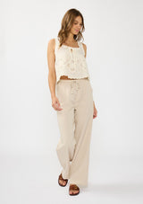 [Color: Cream/Natural] A front facing image of a brunette model wearing a beige eyelet tank top with a square neckline, tie detail, and a scalloped trim. 