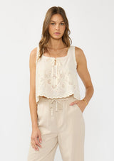 [Color: Cream/Natural] A front facing image of a brunette model wearing a beige eyelet tank top with a square neckline, tie detail, and a scalloped trim. 