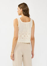 [Color: Cream/Natural] A back facing image of a brunette model wearing a beige eyelet tank top with a square neckline, tie detail, and a scalloped trim. 