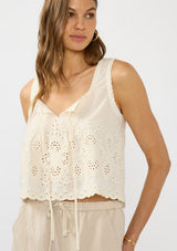 [Color: Cream/Natural] A front facing image of a brunette model wearing a beige eyelet tank top with a square neckline, tie detail, and a scalloped trim. 
