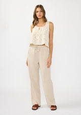 [Color: Sand] A front  facing image of a brunette model wearing a tencel blend beige drawstring pant with an elastic waistband and side pockets. Styled with a beige eyelet tank top. 
