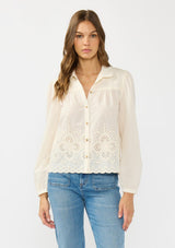 [Color: Cream/Natural] A front facing image of a brunette model wearing an off white embroidered shirt with a collared neck and button front. 