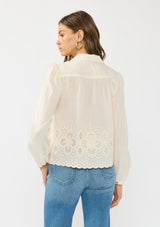 [Color: Cream/Natural] A back facing image of a brunette model wearing an off white embroidered shirt with a collared neck and button front. 