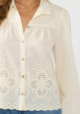 [Color: Cream/Natural] A detail image of a brunette model wearing an off white embroidered shirt with a collared neck and button front. 