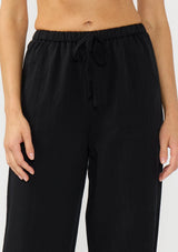 [Color: Black] A detail image of a model wearing a black tencel blend drawstring pant with an elastic waistband and side pockets. 