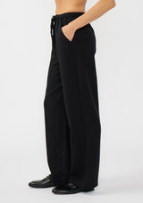 [Color: Black] A side facing image of a model wearing a black tencel blend drawstring pant with an elastic waistband and side pockets. 