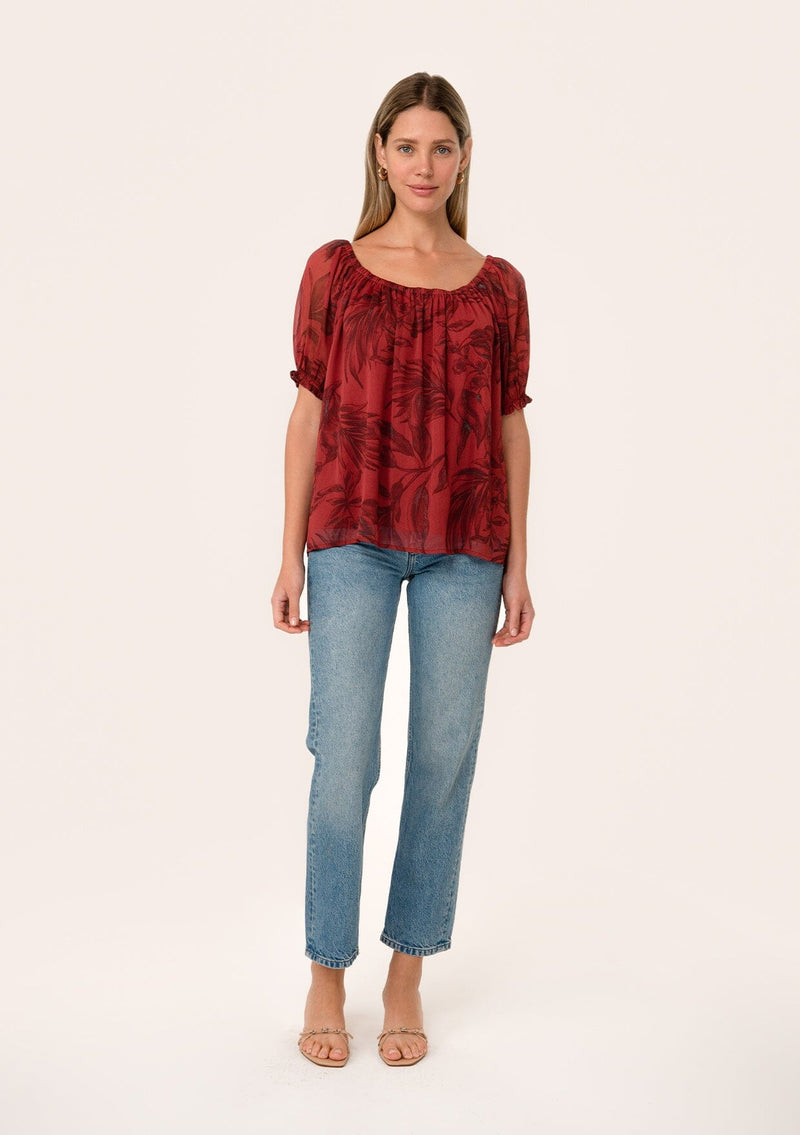 [Color: Wine/Charcoal] A front facing image of a blonde model wearing a fall chiffon blouse in a dark red floral and leaf print. With short puff sleeves, an elastic round neckline, and a relaxed, flowy fit. 