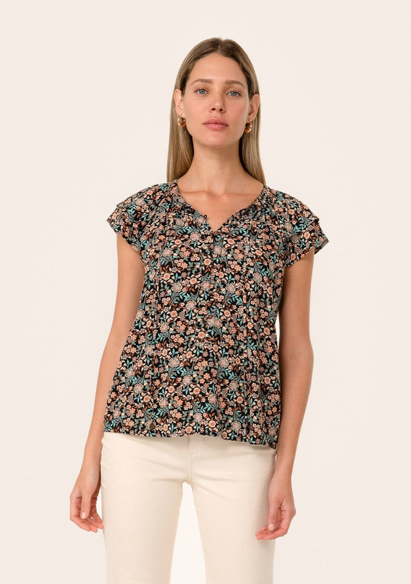 [Color: Black/Teal] A front facing image of a blonde model wearing a bohemian fall blouse in a black and teal floral print. With a self covered button front, double flutter short cap sleeves, and neck ties. 