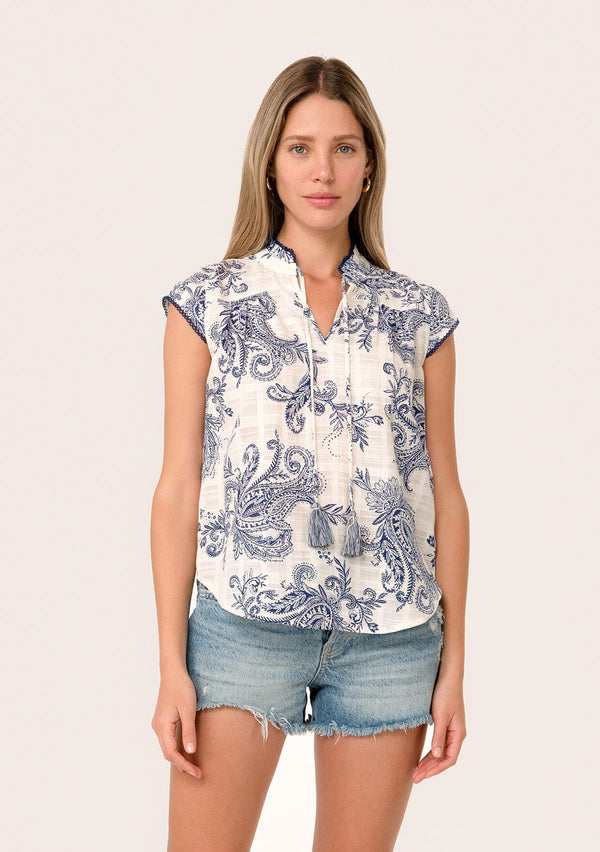 [Color: White/Navy] A front facing image of a blonde model wearing a summer top in a blue and white vintage floral print. With short cap sleeves, a split v neckline with tassel ties, and a contrast crochet edge stitch trim. 