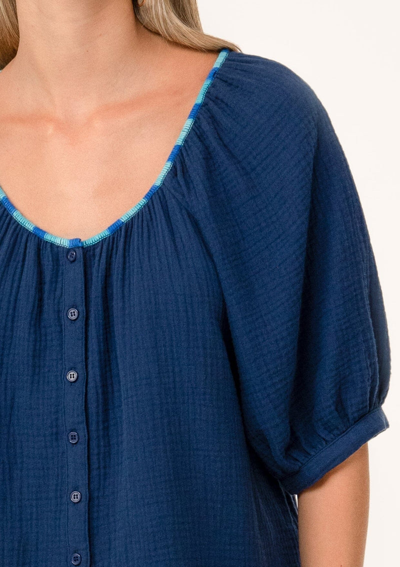 [Color: Navy] A close up front facing image of a blonde model wearing a navy blue cotton gauze blouse. With short raglan puff sleeves, a round neckline with contrast thread details, and a button front. 