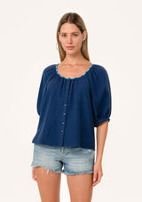 [Color: Navy] A front facing image of a blonde model wearing a navy blue cotton gauze blouse. With short raglan puff sleeves, a round neckline with contrast thread details, and a button front. 