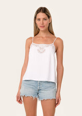 [Color: Chalk] A front facing image of a blonde model wearing a white bohemian camisole with adjustable spaghetti straps, a scoop neckline, a button up back, and lace detail.