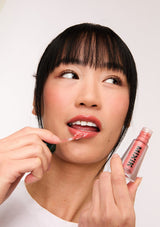 [Color: Apricot] A brunette model holding the Mixik lip plumping ampoule in apricot.