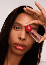 [Color: Vivid Coral] A brunette model holding a Mixik lip tint in bright coral.