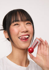 [Color: Spiced Sangria] A brunette model holding a Mixik lip tint in pink.