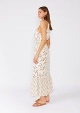 [Color: Latte/Natural] A side facing image of a brunette model wearing an dreamy bohemian maxi dress in an ivory and brown print. With spaghetti straps, a high neckline, a front keyhole detail, a tie neckline, an elastic waist, a tiered flowy skirt, and ladder stitch details throughout. 