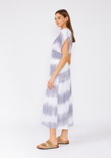 [Color: Off White/Grey] A side facing image of a brunette model wearing a bohemian mid length spring dress in a white and grey stripe. With short dolman sleeves, adjustable ties at the shoulder, an elastic waist, and a double v neckline in the front and back. 
