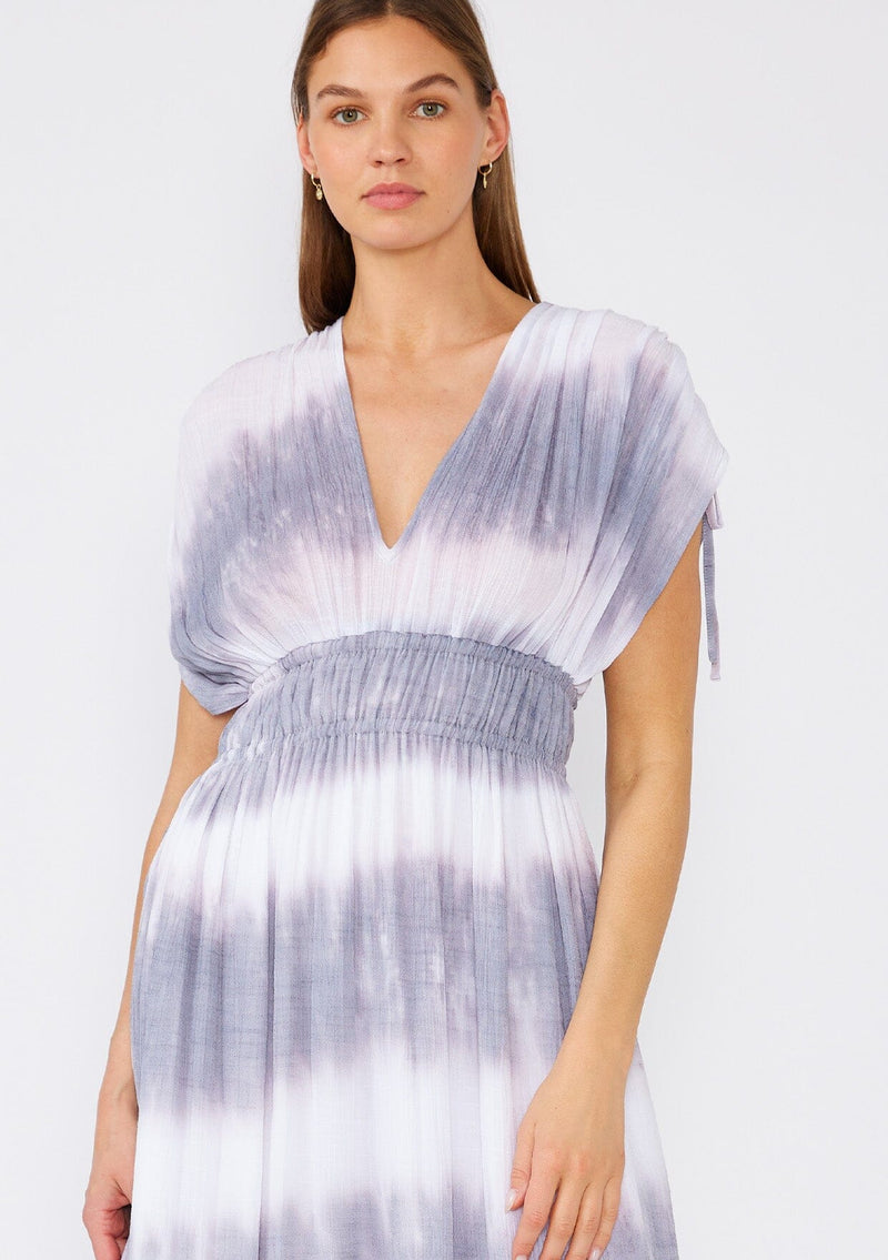 [Color: Off White/Grey] A close up front facing image of a brunette model wearing a bohemian mid length spring dress in a white and grey stripe. With short dolman sleeves, adjustable ties at the shoulder, an elastic waist, and a double v neckline in the front and back. 