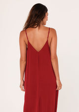 [Color: Brick Red] A back facing image of a brunette model wearing a red harem maxi dress. This billowy maxi tank top dress features a deep v neckline, adjustable spaghetti straps, and a cocoon fit.