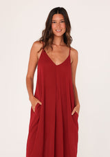 [Color: Brick Red] A close up front facing image of a brunette model wearing a red harem maxi dress. This billowy maxi tank top dress features a deep v neckline, adjustable spaghetti straps, and a cocoon fit.