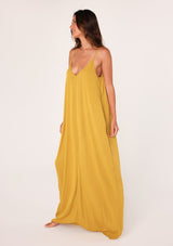 [Color: Mustard] A side facing image of a brunette model wearing a mustard yellow harem maxi dress. This billowy maxi tank top dress features a deep v neckline, adjustable spaghetti straps, and a cocoon fit.