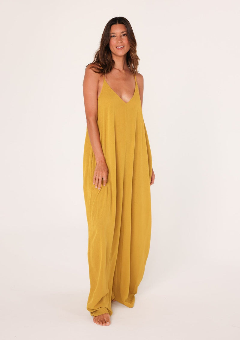 [Color: Mustard] A front facing image of a brunette model wearing a mustard yellow harem maxi dress. This billowy maxi tank top dress features a deep v neckline, adjustable spaghetti straps, and a cocoon fit.