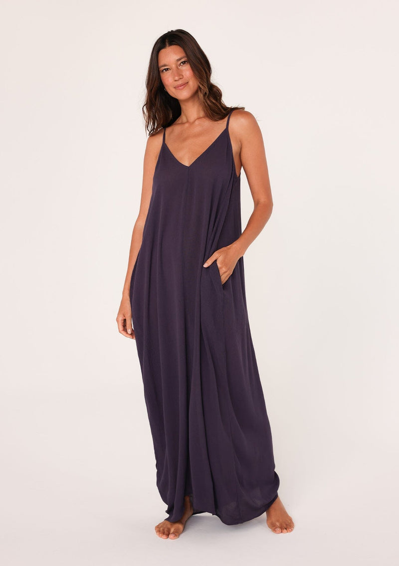 [Color: Dark Purple] A front facing image of a brunette model wearing a dark purple harem maxi dress. This billowy maxi tank top dress features a deep v neckline, adjustable spaghetti straps, and a cocoon fit.
