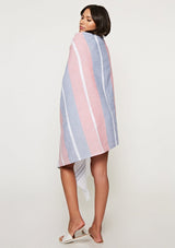 [Color: Red/Navy Stripe] A brunette model with a red and navy stripe beach towel with fringe trim. A cotton towel perfect for lounging by the shoreline or staying dry. 
