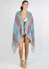 A woman modeling a lightweight patterned beach towel, worn open over a white bikini top and denim shorts.