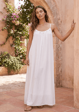 [Color: Off White] A front facing image of a brunette model wearing a white maxi dress with a relaxed fit, scoop neckline with crochet ball trim, and adjustable spaghetti straps. 